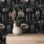 Samolepljiva tapeta kredom vino i suhomesnato na crnoj tabli iza komode od svetlog drveta sa keramičkom vazom