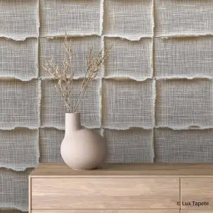 Beige rounded vase with dried stems on a light wood dresser against a textured, grid-like fabric wall backdrop.