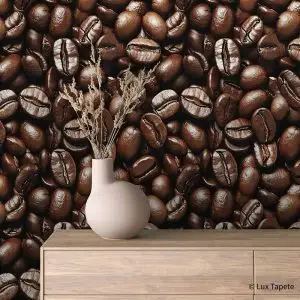 Beige vase with dried stems on a light wood dresser against a wall covered in roasted coffee beans.